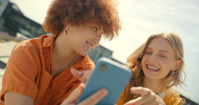 Two women discuss and laugh about something on a mobile phone