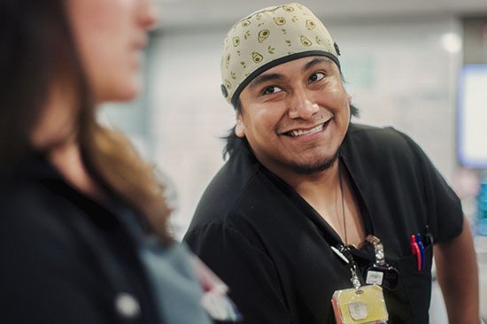 A medical tech smiles as he listens to a colleague speak
