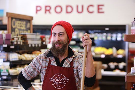 A Sedr-Woolley Woolley market employee holds a cleaning tool and smiles at something in the foreground