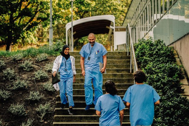 Two medical professionals in scrubs walking down stairs outside and smiling