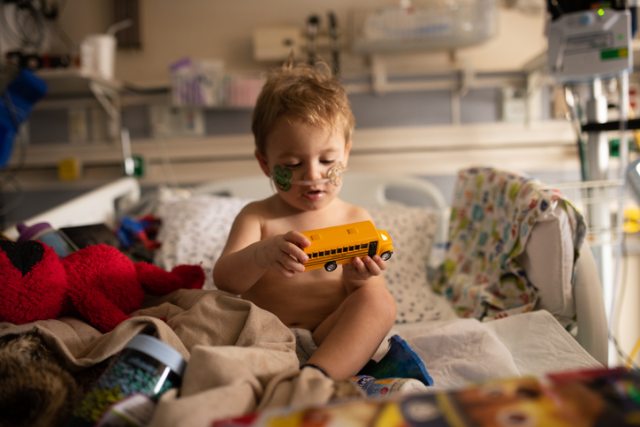 Child playing with a school bus toy in a hospital bed