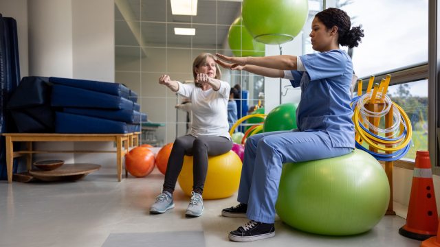 therapist uses balance ball to show exercise to a woman patient