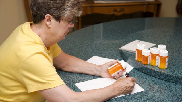 Woman writes on paper with bottles of pills nearby