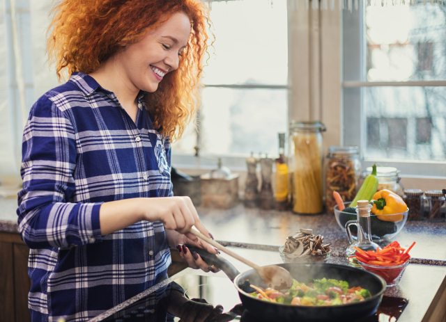 Smiling woman stirs veggies in pan on the  stove