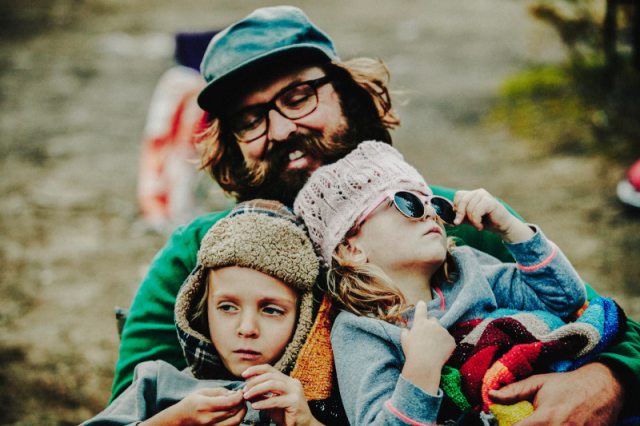 Father holding two children in his arms and smiling down at them. 