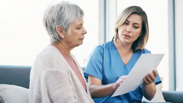 Nurse showing test results to senior woman on paper and talking, discussing and sharing treatment options in old age home. Caregiver, caretaker or medical healthcare professional helping elderly lady