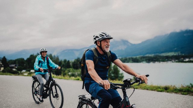 An older couple ride bicycles down a concrete path near a body of water