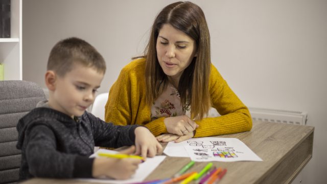 Young child draws on paper while sitting next to young woman
