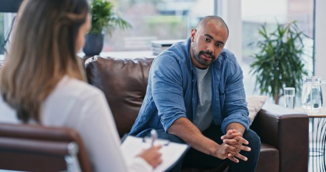 man with a mustache sitting on a couch talks to a therapist