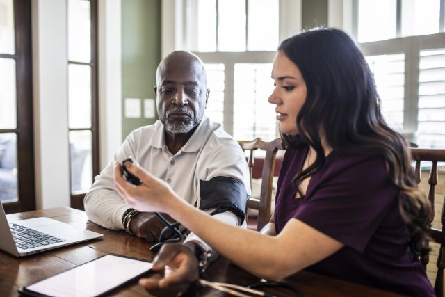 Home care worker takes blood pressure of man at table