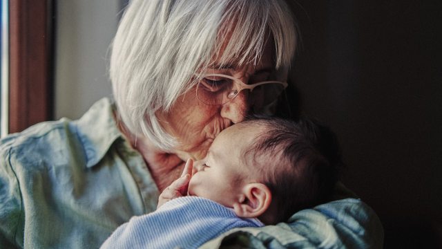 An older woman kisses the forehead of a newborn baby