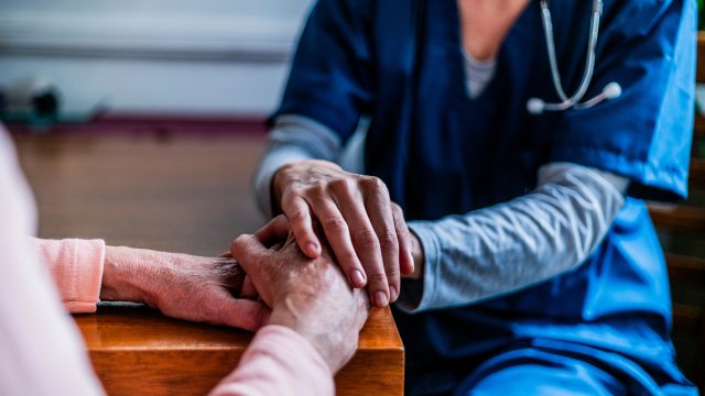 A caregiver holds the hands of an elderly patient