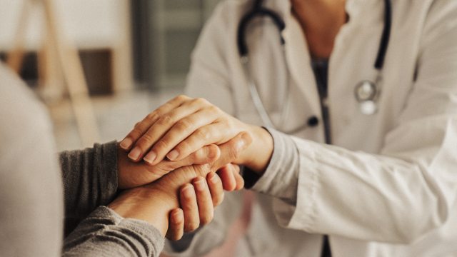 A caregiver holds a patient's hand in a clinical setting as a show of comfort