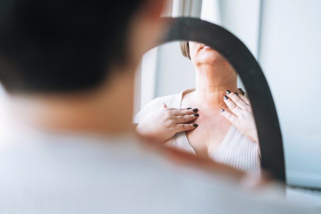 woman looks into mirror and touches front of neck