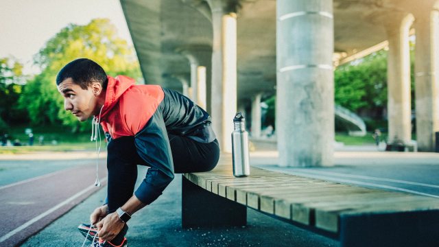A man sits on a concrete platform and laces up his shoes in preparation for a run