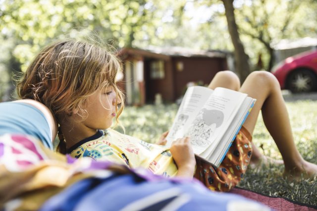 young person reads a book outside in summer