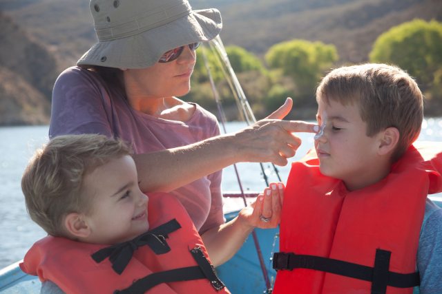 woman puts sunscreen on face of boy in a boat