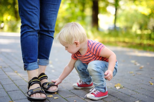 small child bends to touch the sandals of an adult in a parklike setting