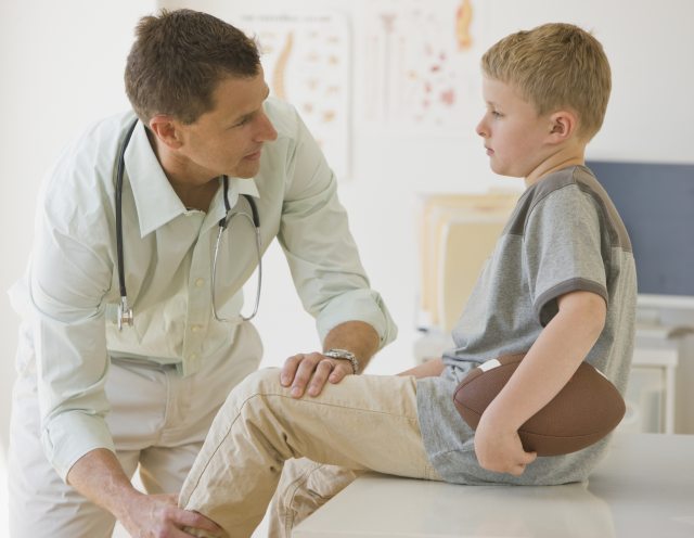 doctor examines leg of young boy with football