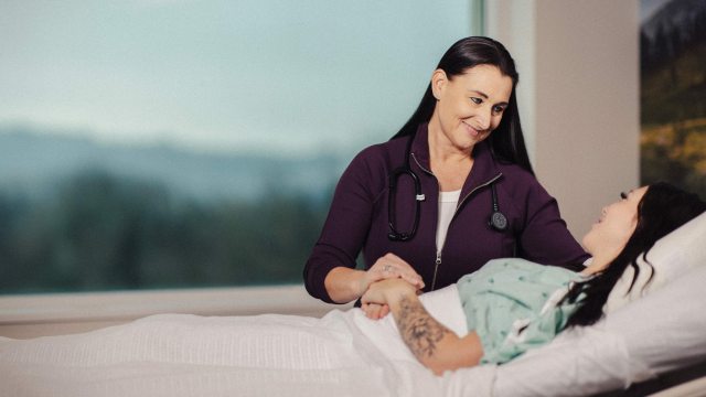 A caregiver sits bedside and comforts patient in a clinical setting