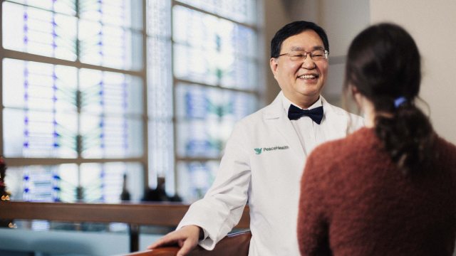 A PeaceHealth provider smiles and listens to a patient in the foreground