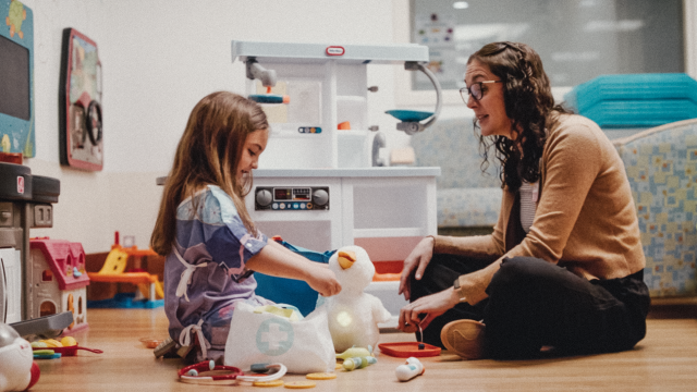 A caregiver sits, plays and talks with a young patient in a warm clinical setting