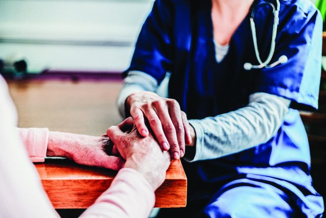 A caregiver and person in the foreground with clasped hands