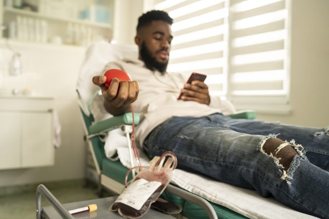 Man donates blood, squeezes red ball while lying on clinic chair