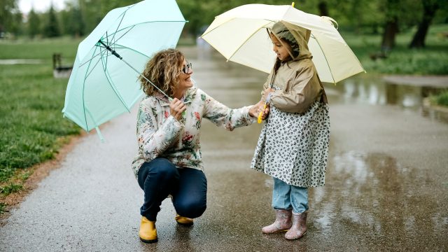 A woman and young girl with umbrellas walking on a sidewalk in the rain