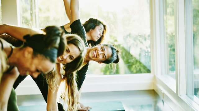 A group of women in a well lit room, laugh and smile during a yoga session