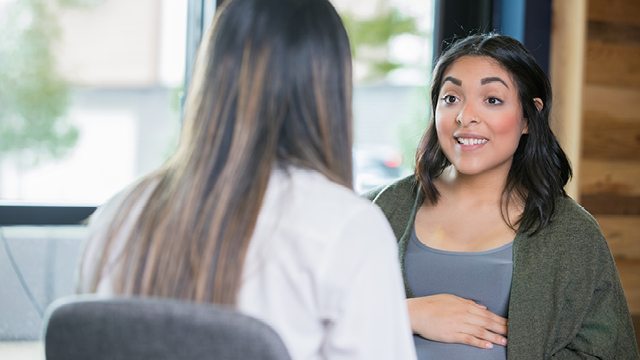 A caregiver with her back to the camera speaks with an expecting mother