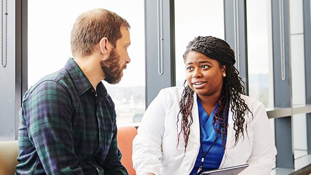 A caregiver speaks with a patient in a clinical lobby