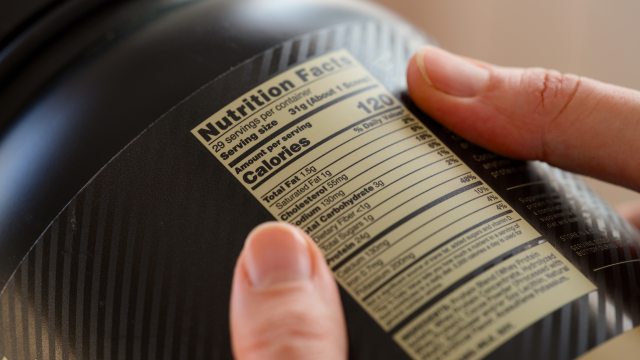 close-up of hands holding jar to examine nutrition label