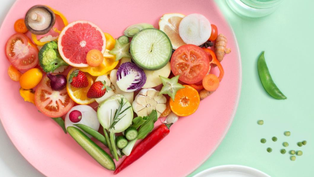 Healthy array of fruits and vegetables, arranged in the shape of a heart, on a pink plate