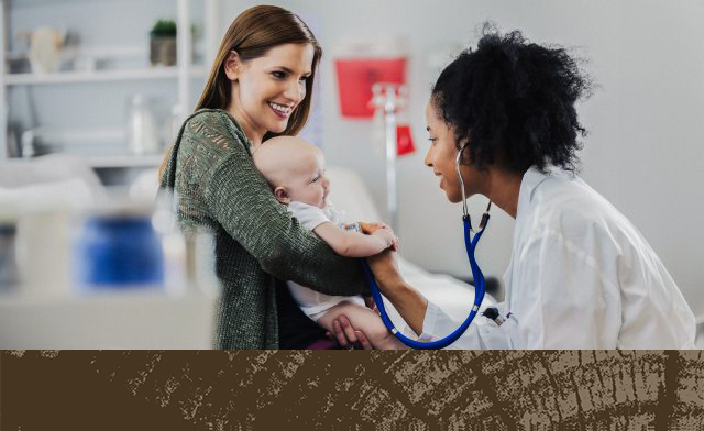 A mother holds her baby while a caregiver examines the child with a stethoscope in a clinical setting