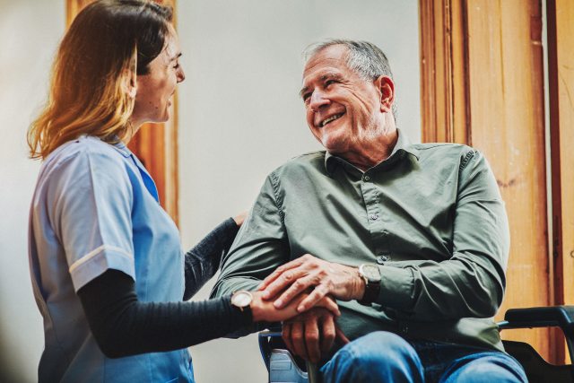 A caregiver smiles and comforts a patient in a clinical setting
