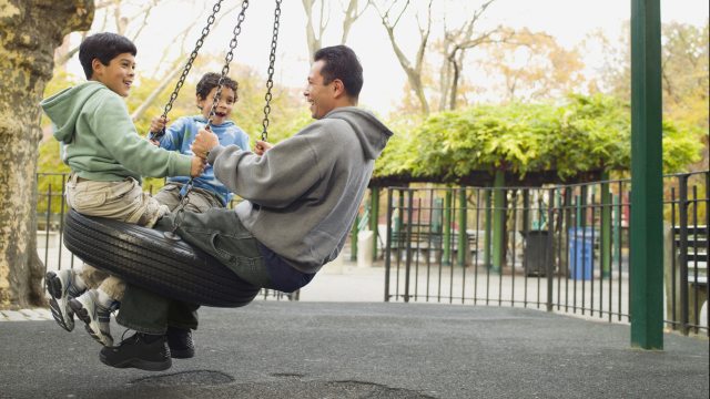 Dad and two young boys play on tire swing at park