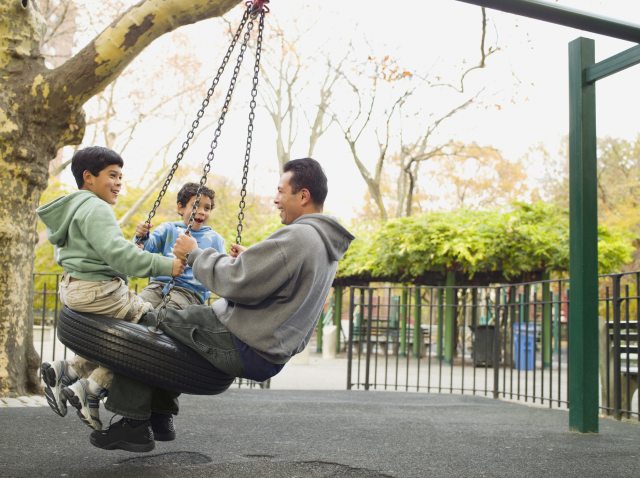 Dad and two young boys play on tire swing at park