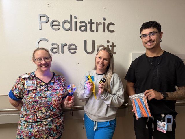 3 pediatric nurses holding up donated toys and smiling at the camera