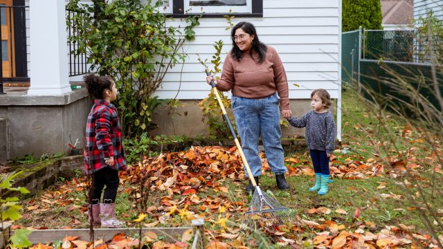 Mom and two children rake leaves in front of house