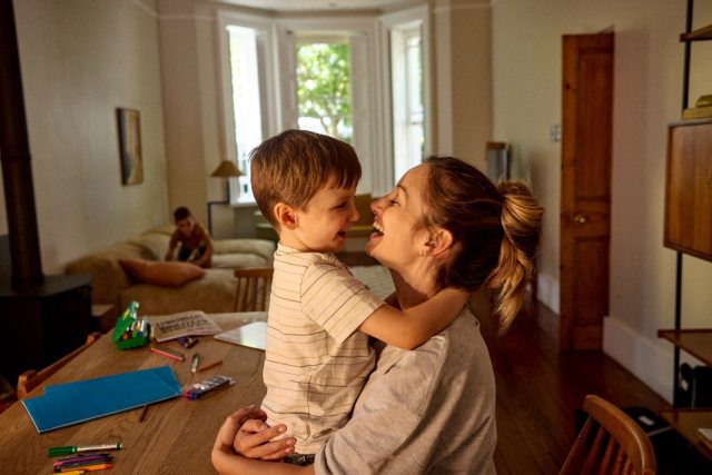 A woman holding a child and smiling at him in their home