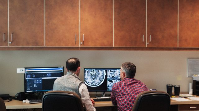 Two caregivers examining a brain scan image on a computer monitor