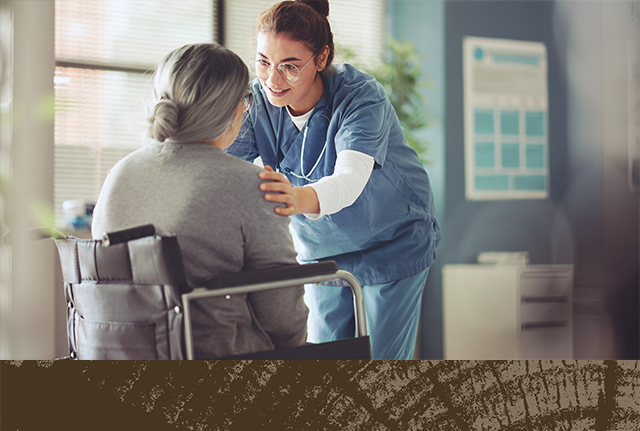 A nurse comforts an older person sitting in a chair in the foreground