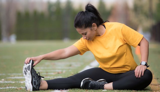 A woman in yellow shirt and black pants stretching on a field in preparation for exercise
