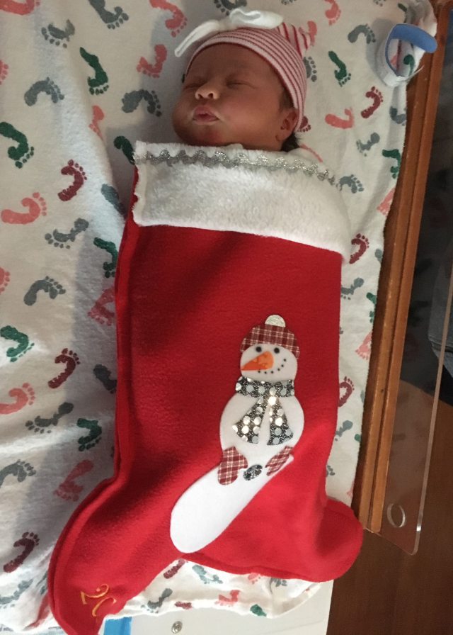 A sleeping newborn baby wrapped in a holiday stocking 