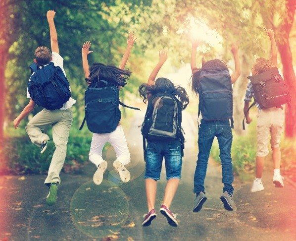 Kids wearing backpacks jump in the air in excitement
