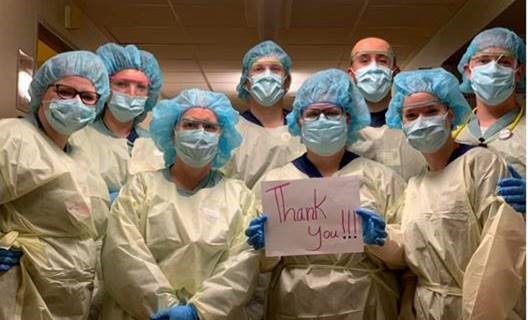 A group of caregivers in surgery scrubs holds a sign that reads, "Thank you!!!"