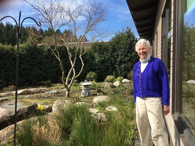 Carolyn Haugen stands near a garden on a sunny day