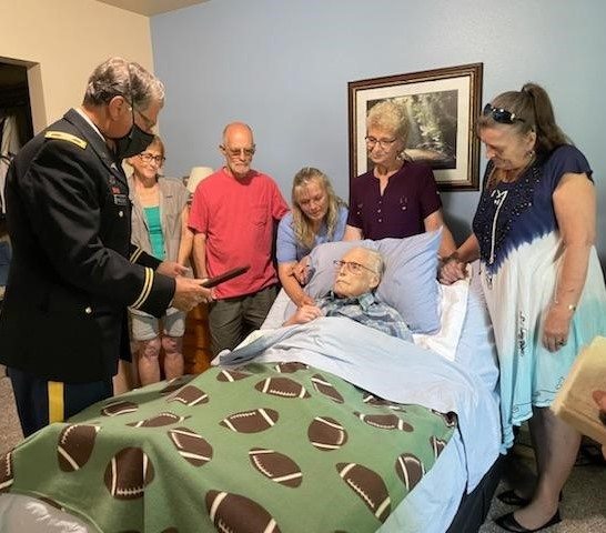A Veteran being pinned with a medal while in a hospital bed, with family and friends around him.