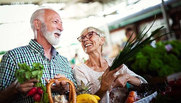 An older couple smiles and talks while shopping for produce